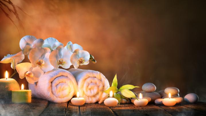 Towel on fern with candles and brown hot stone on wooden background.
